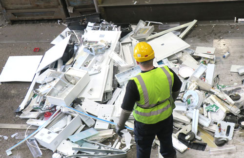 A recycling plant operative in a hard hat assesses some waste lights